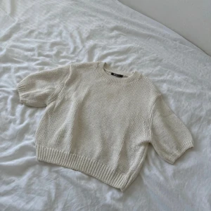 Beige stickad tröja Gina Tricot - Superfin beige stickad tröja från Gina Tricot med korta ärmar och rund hals. Tröjan har en chunky stickning och ribbade muddar vid ärmslut och nederkant. Perfekt för lager-på-lager och passar till både jeans och kjol.