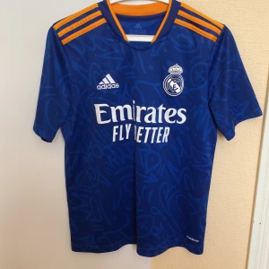 Real Madrid 21/22 bortatröja Adidas - Real Madrid 21/22 säsongens borta tröja i barn storlek L, 158/164. Använt den ganska mycket men är fortfarande i ett bra skick. Gillar tröjan väldigt mycket men är tyvärr för liten nu för mig.
