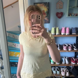 Ljusgul T-shirt  - Supersöt ljusgul blus från Hollister med korta ärmar och v-ringning. Nedtill finns en bred spetskant som ger en romantisk vibe. Tunt och mjukt bomullstyg, perfekt för varma dagar. Liten broderad Hollister-logga framtill.