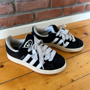 Adidas Campus sneakers svart/vit mocka - Svarta Adidas Campus sneakers i mocka med vita detaljer och klassiska tre ränder på sidorna. Tjocka vita snören och vit sula. Svarta snören tillkommer även. Väl använda men i fint skick, lite sliten på insidan