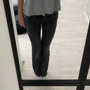 Svarta bootcut jeans med fickdetaljer - Snygga svarta bootcut jeans med två knappar i midjan och coola fickor med lock och knapp bak. Jeansen har en lätt tvättad look och sitter tajt upptill med utsvängda ben. Perfekta för dig som gillar en trendig och avslappnad stil. Inte användt så mycket💕