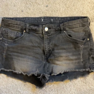 Svarta jeansshorts med fransig kant - Snygga svarta jeansshorts med fransig rå kant och slitningar framtill. Klassisk femficksmodell med knapp och dragkedja. Perfekta för sommaren och ger en cool vibe till din outfit.