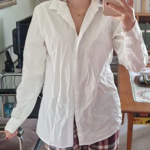 Vit skjorta från H&M, strl 170 - Klassisk vit skjorta från H&M i storlek 170. Skjortan har lång ärm, knappar framtill och en snygg krage. Tillverkad i bomull, perfekt för en clean och stilren look. Passar dig som gillar enkel och tidlös stil.