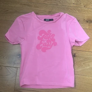 Rosa t-shirt från Bik Bok med tryck - Snygg rosa t-shirt från Bik Bok med coolt 'Take it Easy'-tryck framtill. Modellen är kortärmad och har en klassisk rund halsringning. Tillverkad i mjuk bomull med lite stretch för skön passform. Perfekt för dig som gillar färg och statement-prints!