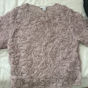 Ljusrosa blus med 3D-blommor från Amisu - Supersöt ljusrosa blus från Amisu i mesh med massor av 3D-blommor över hela plagget. Blusen har rund halsringning och halvtransparent material som ger en unik och romantisk look. Perfekt för dig som vill sticka ut med en cool och feminin stil.