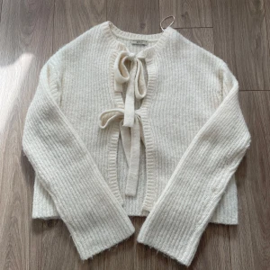 Vit ribbad kofta med knyt rosetter  - Supermysig vit kofta från Gina tricot med ribbad struktur och två stora knytband framtill. Koftan är stickad i mjukt material och har långa ärmar med lite loose passform. Perfekt nu till höst. Använd tre gånger