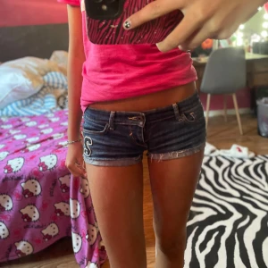 Mörkblå jeansshorts Abercrombie - Snygga mörkblå jeansshorts från Abercrombie & Fitch med låg midja och fransade kanter. Shortsen har broderad siffra '2' och a&f på ena benet, klassiska fickor och coola sömmar bak. Perfekta för sommarens alla häng!