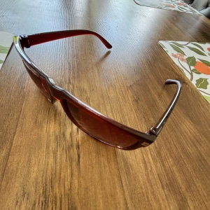 Ray bans boyfriend liknade - Snygga solglasögon med fyrkantig form och bruna bågar samt tonade bruna glas. Ramen är i plast och har en stilren look med små silvriga detaljer vid hörnen. Perfekta för att ge din outfit en cool touch i solen. Liknade ray bans