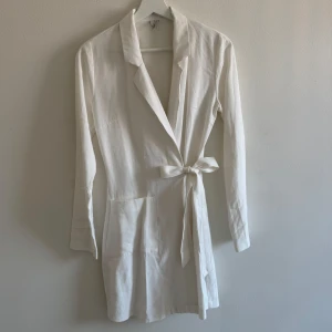 Vit kostymklänning omlott från NLY Trend - Snygg vit kavajklällimg från NLY Trend i omlottmodell med knytband i midjan. Långärmad och med klassisk krage, perfekt för en clean och stilren look. Vit långärmad wrap kostym klänning från Nelly.com. Använd varsamt, ser inga skavanker. Knapp innuti för o fästa wrapen samt knytdetalj. Fickor på framsidan. Jag har massor av artiklar till salu! Köp flera och få rabatt!