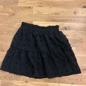 Svart prickig volangkjol från SHEIN - Supersöt svart kortkjol från SHEIN med volanger och prickigt mönster. Kjolen har en smockad midja som är både bekväm och snygg, samt ett lätt och luftigt tyg.