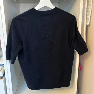 Mörkblå kashmirtröja från H&M - Snygg mörkblå tröja från H&M i mjuk kashmir. Modellen har rund hals och korta ärmar, perfekt för dig som gillar stilrena och enkla plagg. Passformen är normal och materialet känns lyxigt mot huden. En klassiker som funkar till jeans eller kjol.