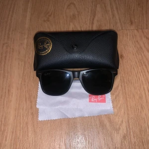 Svarta Ray-Ban  solglasögon - Snygga svarta Ray-Ban Wayfarer solglasögon med mattsvart båge och mörka glas. Klassisk fyrkantig form och diskret Ray-Ban-logo på sidan. Kommer med originalfodral och putsduk. Perfekta för att lyfta din stil i solen.
