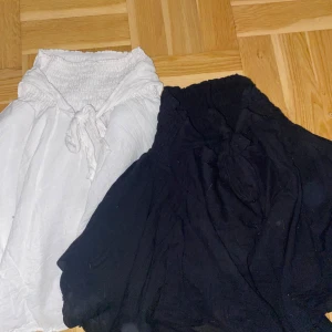 Svart och vit kortkjol med knyt - Två fluffiga korta kjolar i svart och vitt med bred smock i midjan och knytband framtill. Märke vet ej, kan oxå andvändas som tröja 
