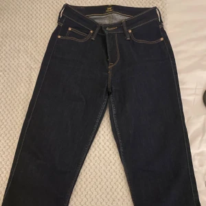 Mörkblå jeans från Lee - Säljer ett par klassiska mörkblå jeans från Lee med raka ben och snygga kontrastsömmar. Jeansen har fem fickor och gylf med dragkedja. Perfekta för dig som gillar en tidlös och clean look.