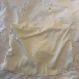 Ljusbeige linnetopp med smala band - Säljer en stilren ljusbeige linnetopp med smala axelband och v-ringad hals. Toppen har en enkel och clean look, perfekt att matcha med jeans eller kjol. Materialet känns mjukt och har en lätt glansig yta.