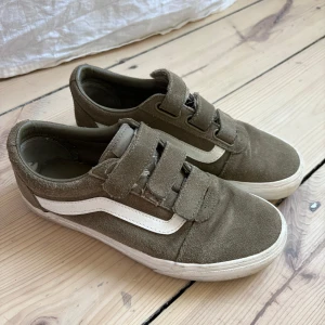 Olivgröna Vans sneakers med kardborre - Snygga olivgröna Vans sneakers i mocka med klassisk vit sidorand och vit sula. Skorna har tre breda kardborreband för enkel påtagning och en låg profil. 