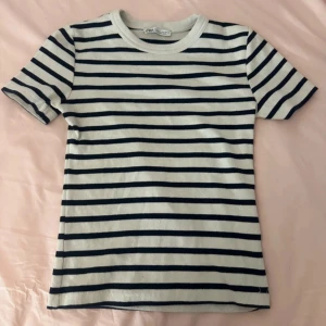 Randig t-shirt från Zara - Snygg randig t-shirt från Zara i vit och marinblå. Klassisk rund hals och korta ärmar. Ribbad bomull som är mjuk och skön mot huden. Perfekt för dig som gillar enkel och stilren design med lite edge.