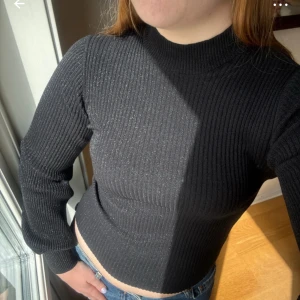 Svart ribbad tröja Samsøe Samsøe 36/S - Svart ribbad polotröja från Samsøe Samsøe med tight passform och lång ärm. Tröjan har en hög krage och är stickad i mjukt material som sitter snyggt mot kroppen. Perfekt att matcha med jeans eller kjol för en clean look. Storlek 36/S. Tröjan är lagad i halsen, se bild. 