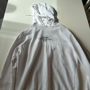 Vit Purpose Tour hoodie från Bieber - Säljer en vit hoodie från Justin Biebers Purpose World Tour 2016. Tröjan har tryck med turnéns namn fram och bak samt turnéstäder längs ena ärmen. Mjuk insida i fleece, huva med snörning och långa ärmar. Perfekt för dig som älskar streetwear och musikmerch.