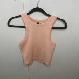 Ljusrosa ribbad croppad linnetopp H&M - Superfin ljusrosa croppad linnetopp från H&M Divided. Toppen är ribbad och ärmlös med breda axelband och rund halsringning. Perfekt för varma dagar eller att styla lager på lager. Enkel och stilren design som passar till allt.