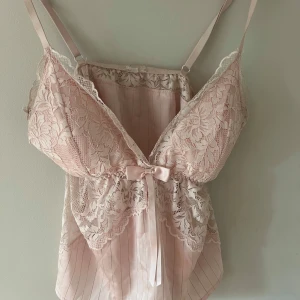 Ljusrosa spetsig linnetopp med rosett - Superfin ljusrosa linnetopp med spetsdetaljer och tunna axelband. Toppen har en liten rosett framtill och är ifrån newyorker i storlek XS/S. Kommer inte till användning längre. 