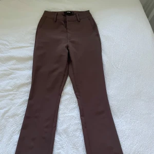 Vilma kostymbyxor bruna  - Snygga bruna kostymbyxor från bikbok med bootcut-ben och hög midja. Byxorna har klassiska fickor fram, hällor för bälte och stängs med dragkedja och knapp. Perfekta för en clean och stilren look.