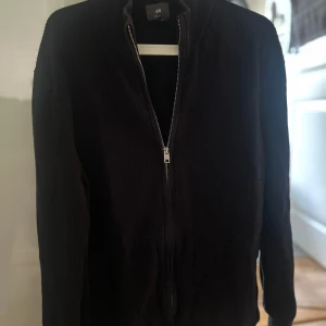 Svart stickad cardigan jacka - Svart stickad cardigan jacka från H&M med hel dragkedja framtill. Jackan har en enkel, clean look med ribbade detaljer längs ärmar och krage. Perfekt för lager-på-lager och chill vardagsstil.