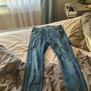 Levi's 501 blå jeans straight fit - Klassiska Levi's 501 jeans i blå denim med rak passform och fem fickor. Snyggt slitna detaljer och ikonisk röd Levi's-tag på bakfickan. Perfekt för dig som gillar tidlös stil och vill ha ett par jeans som funkar till allt. 32/32 storlek 