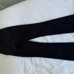 Vilma kostymbyxor svart  - Snygga svarta kostymbyxor med rak passform och klassisk design. Byxorna har midja med hällor och diskreta fickor. Perfekta för en clean och stilren look. Materialet känns mjukt och följsamt.