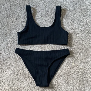 Svart ribbad bikini med bikini topp,aldrig använt. - Snygg svart bikini med ribbad struktur och sportig topp med breda axelband. Underdelen har klassisk midja och enkel design. Perfekt för stranden eller poolen. Materialet är stretchigt och bekvämt.
