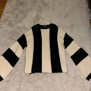 Randig stickad tröja i svart och vitt - Säljer en stickad tröja med breda svarta och vita ränder. Tröjan har lång ärm och rak passform, perfekt för dig som gillar en stilren och trendig look. Mjuk och skön att bära, passar till många outfits.