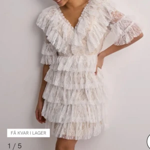 By malina birger klänning  - Superfin vit kortklänning i spets med flera lager volanger och v-ringad hals. Klänningen har trekvartsärm med volangdetaljer och ger en romantisk och drömmig vibe. Perfekt för dig som vill sticka ut med en feminin look och älskar detaljer.