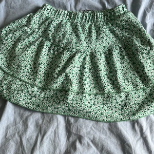 Gröna blommiga shorts från Zara - Säljer ett par gröna shorts från Zara med sött blommigt mönster i vitt och svart. Modellen har hög midja med resår och är gjorda i ett mjukt, strukturerat bomullstyg. Perfekta för varma dagar och har en skön passform som känns chill.