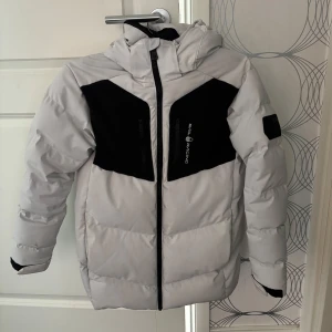 Sail Racing vinter jacka - Snygg vinterjacka från Sail Racing i vit med svarta detaljer på bröstet och luva. Perfekt för kalla dagar med sin tjocka och vadderade design. Använd 1 vinter men där av priset💕