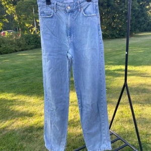 Bershka High Waist Straight Jeans - Ljusblå high waist jeans från Bershka i rak modell. Klassisk femficksdesign, röda kontrastsömmar och råa benslut för en chill vibe. Tillverkade i denim med snygg tvätt och diskret slitning på bakfickan.