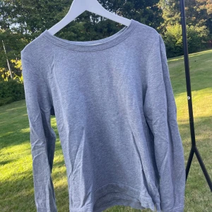 Grå långärmad tröja Vero Moda - En enkel och stilren grå långärmad tröja från Vero Moda i storlek L men passar till M och S. Tröjan har rund halsringning och är gjord i mjuk bomullsmix som är skön mot huden. Perfekt att slänga på sig när det är lite kyligt ute. Passar dig som gillar basic och clean look.