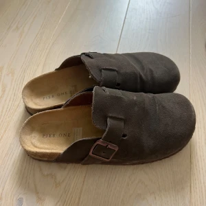 Bruna mockatofflor från Pier One - Mörkbruna slip-in tofflor från märket Pier One i mjuk mocka. Säljer då jag inte använder dem. Köpta förra sommaren och endast använda ett fåtal gånger. Storlek 41. Köpta för 449 kr, mitt pris 300 kr. Köparen står för frakten🫶🏻