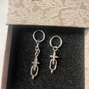 Silvriga örhängen med coola detaljer - Säljer ett par silvriga örhängen med hängande detaljer som har en edgy design med små nitar och länkar. Perfekt för dig som vill ha något unikt och trendigt till din stil. Kommer i en snygg ask. Oanvända! Kommer ifrån IOAKU 💞