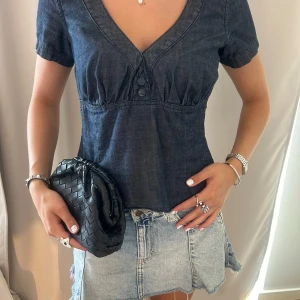 Mörkblå jeansblus med v-ringning - Supersnygg mörkblå jeansblus med markerad v-ringning och två dekorativa knappar framtill. 