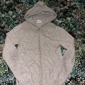 Grå cashmere hoodie från John Henric - Mjuk och lyxig grå hoodie i 100% cashmere från John Henric. Tröjan har dragkedja framtill, huva och långa ärmar. Perfekt för dig som gillar en clean och chill stil med premiumkänsla. Tröjan har en defekt på ryggen men som knappt syns. Priset kan diskuteras vid snabb affär
