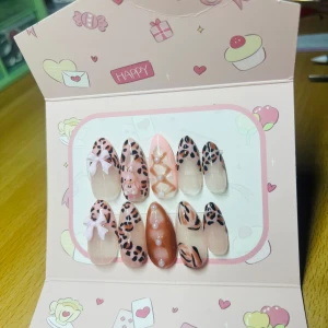 Leopardmönstrade lösnaglar med rosetter - Snygga lösnaglar i mandelform med rosa och nude bas, leopardmönster i svart och brunt, dekorerade med 3D-rosetter, pärlor och korsade band. Mix av transparenta och täckande naglar för en unik look. Perfekt för dig som vill sticka ut med coola detaljer.