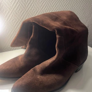 Bruna mockastövlar med låg klack - Snygga bruna stövlar i mjuk mocka med spetsig tå och låg klack. Stövlarna har en klassisk form och är perfekta för dig som gillar en stilren look med lite western-vibe. Passar till både jeans och kjol för en trendig outfit. Storlek 38 och från vero cuoio!