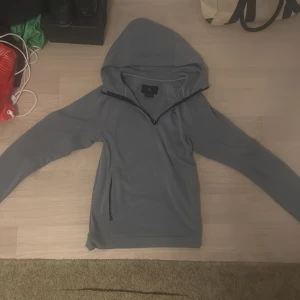 Grå Jordan hoodie med half zip - Säljer en grå hoodie från Jordan med half zip framtill och en ficka med dragkedja på sidan. Tröjan har huva, lång ärm och är gjord i mjukt bomullsmaterial. Perfekt för chill eller träning, snygg logga på bröstet och stilren design. Vid funderingar så är det bara att skriva ✍️ ✅