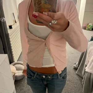Ljusrosa kofta  - Supersöt ljusrosa kofta från Vero Moda med smal passform och långa ärmar. Koftan har knappar framtill och är tillverkad i mjuk bomullsmix. Perfekt att slänga över ett linne eller t-shirt för en chill look.