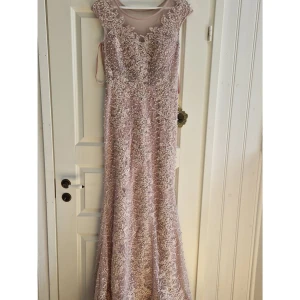 Lång ljusrosa paljettklänning - Magisk långklänning i ljusrosa med massor av paljetter och pärlor. Klänningen har mesh upptill, vackra broderier och en figurnära passform. Perfekt för balen. Detaljerad och glittrig design som verkligen sticker ut. Aldrig använd med lapp kvar!