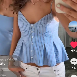 Blå randig linnetopp med knappar - Supersöt blå och vit randig linnetopp med smala axelband och v-ringning. Toppen har knappar framtill och en utsvängd, peplum-liknande nederdel som ger en riktigt snygg siluett. Perfekt för varma dagar och enkel att styla med jeans eller kjol.