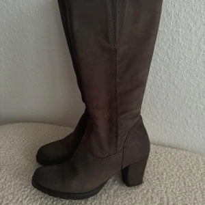 Bruna stövlar med klack - Snygga bruna stövlar med hög skaft och stadig klack. Skorna är gjorda i skinn och har en dragkedja på sidan för enkel på- och avtagning. Rund tå och platt sula ger en bekväm känsla. Perfekt för dig som gillar stilrena och klassiska boots. Insydd gummiband för bredare vader. Använd 3 gånger.