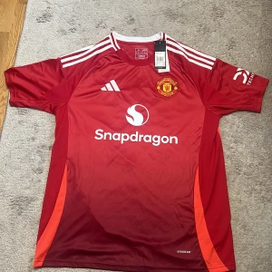 Manchester United Garnacho #17 tröja XL - Manchester United matchtröja från Adidas i röd färg med vita detaljer och tryck. Kortärmad, slim fit och tillverkad i lätt polyester. Garnacho #17 på ryggen, klubbmärke broderat på bröstet och Snapdragon sponsor framtill. Perfekt för dig som vill representera United. Helt ny, oanvänd & autentisk. Tröja från 24/25 säsong.