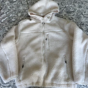 Vit teddyjacka med huva från H&M - Mysig vit teddyjacka från H&M med huva och dragkedja framtill. Jackan har tre fickor med dragkedja och är tillverkad i fluffigt teddy-material som håller dig varm. Perfekt för kyliga dagar och har en avslappnad passform.🥰