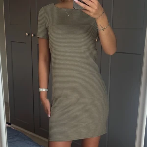 Kort grönrandig klänning med kort ärm - Säljer en enkel och snygg kort klänning i ljusgrön ton med smala horisontella ränder. Klänningen har rund halsringning och korta ärmar. Perfekt för dig som gillar stilrena och bekväma plagg.